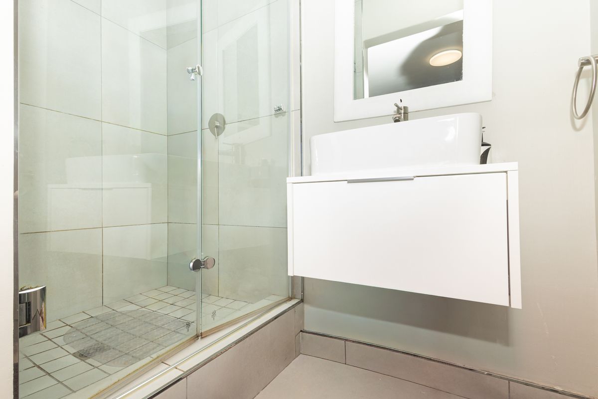 Modern bathroom featuring a glass-enclosed shower, a sleek wall-mounted vanity with a vessel sink, and neutral tiled finishes.