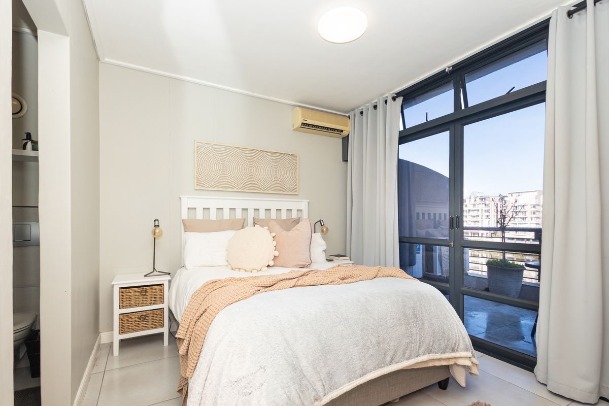 A well-lit bedroom featuring tiled flooring, a wall-mounted air conditioning unit, and large glass sliding doors providing access to an outdoor balcony.