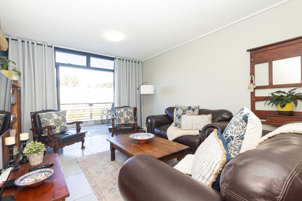 A bright and spacious living room featuring tiled flooring, an air conditioning unit, and large sliding glass doors leading to an outdoor balcony.