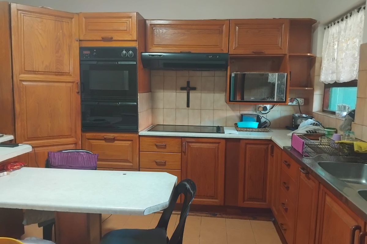A functional kitchen featuring traditional wooden cabinetry, integrated double oven, electric cooktop, and a stainless steel sink with tiled backsplash.