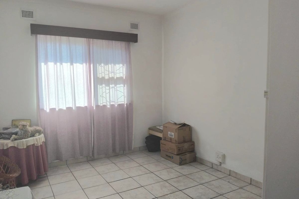 A simple, neutrally painted bedroom featuring tiled flooring and a sliding glass door with security gate access.