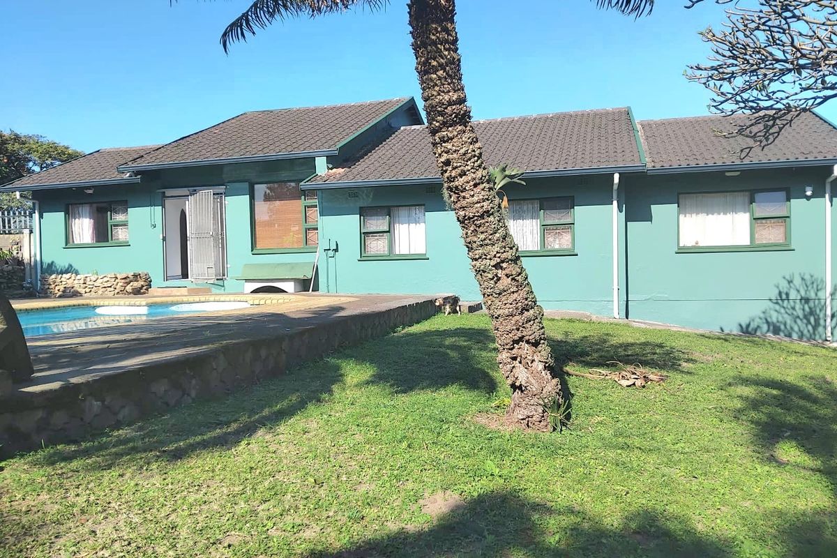 Rear view of the house featuring a swimming pool, stone retaining wall, and a spacious garden area with established palm tree.
