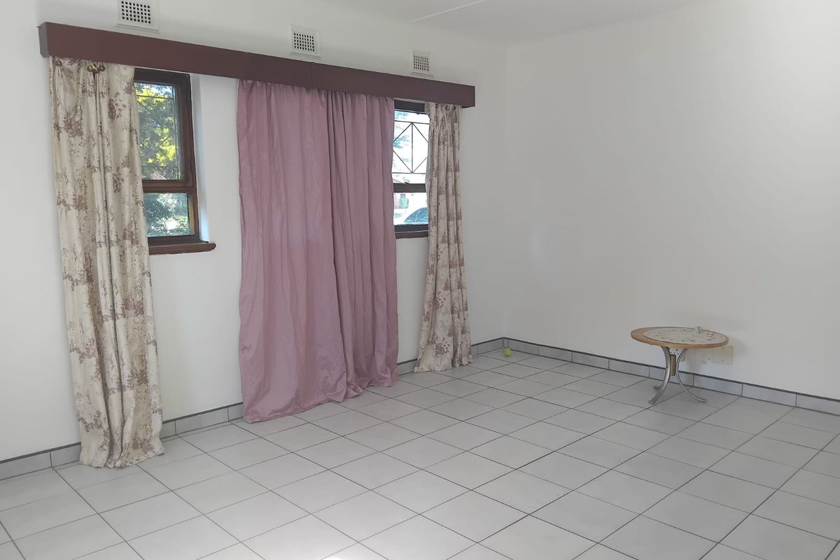 A bright, empty living room featuring neutral tiled flooring and large windows with installed curtain rails, offering a blank canvas for interior design.