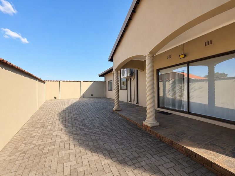 A spacious paved patio area featuring decorative columns, sliding glass doors, and a secure perimeter wall, ideal for outdoor entertaining.