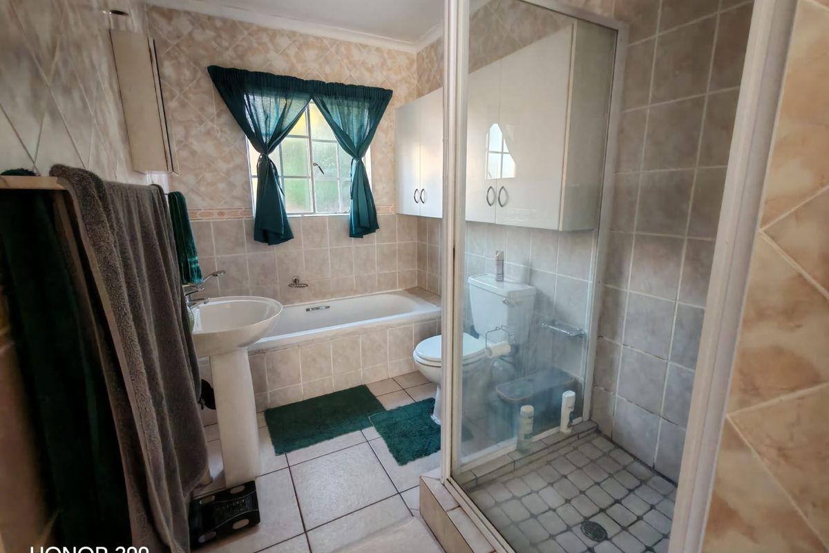 A functional bathroom featuring a pedestal basin, a built-in bathtub, and a separate glass-enclosed shower with wall-mounted cabinetry.