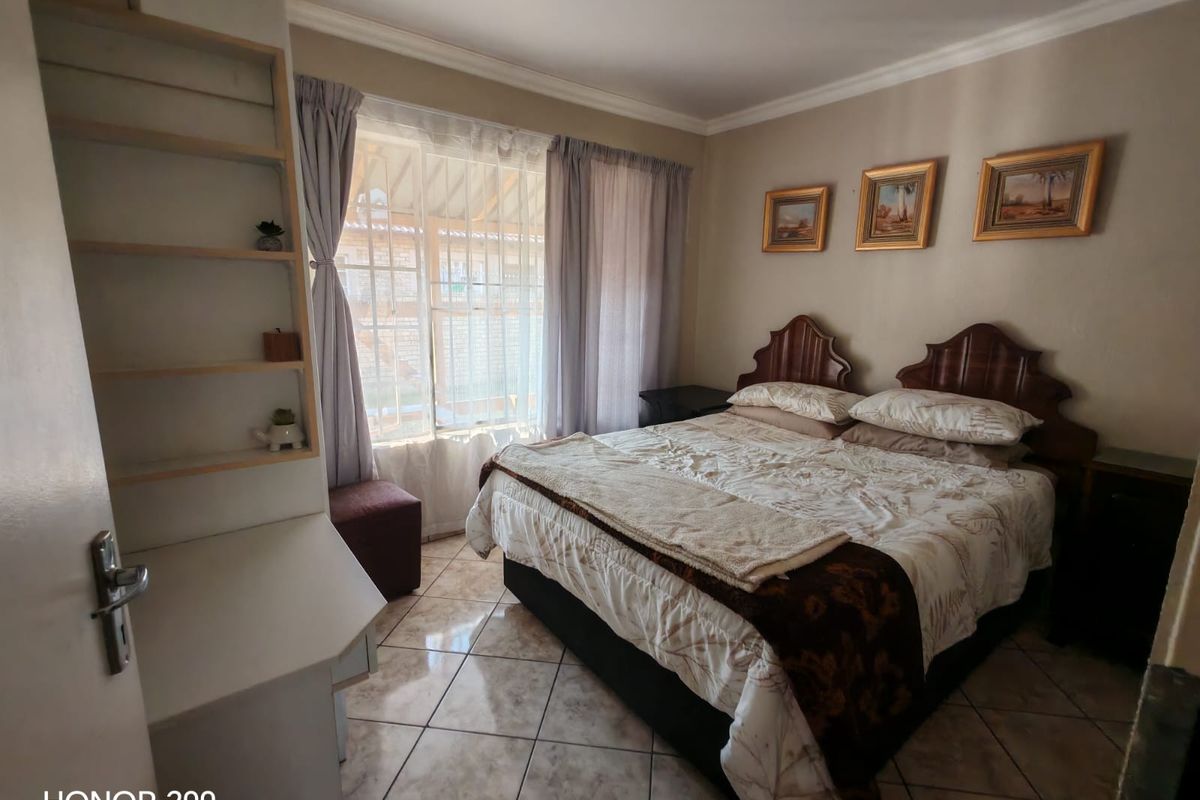 A bedroom featuring tiled flooring, built-in shelving, and large windows with curtains, providing a functional and comfortable living space.