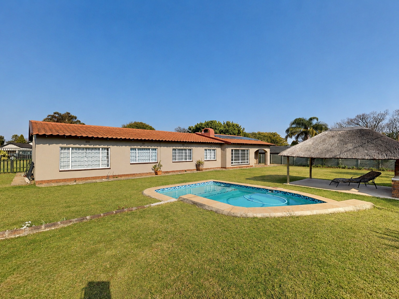 Spacious rear garden featuring a swimming pool, a traditional thatch lapa with a built-in braai, and a well-maintained lawn area.