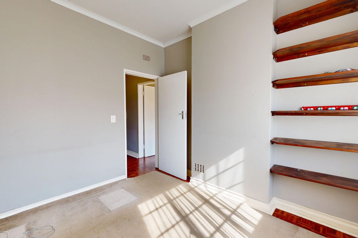 A vacant bedroom featuring neutral walls, built-in wooden shelving, and carpeted flooring, offering a blank canvas for personalization.