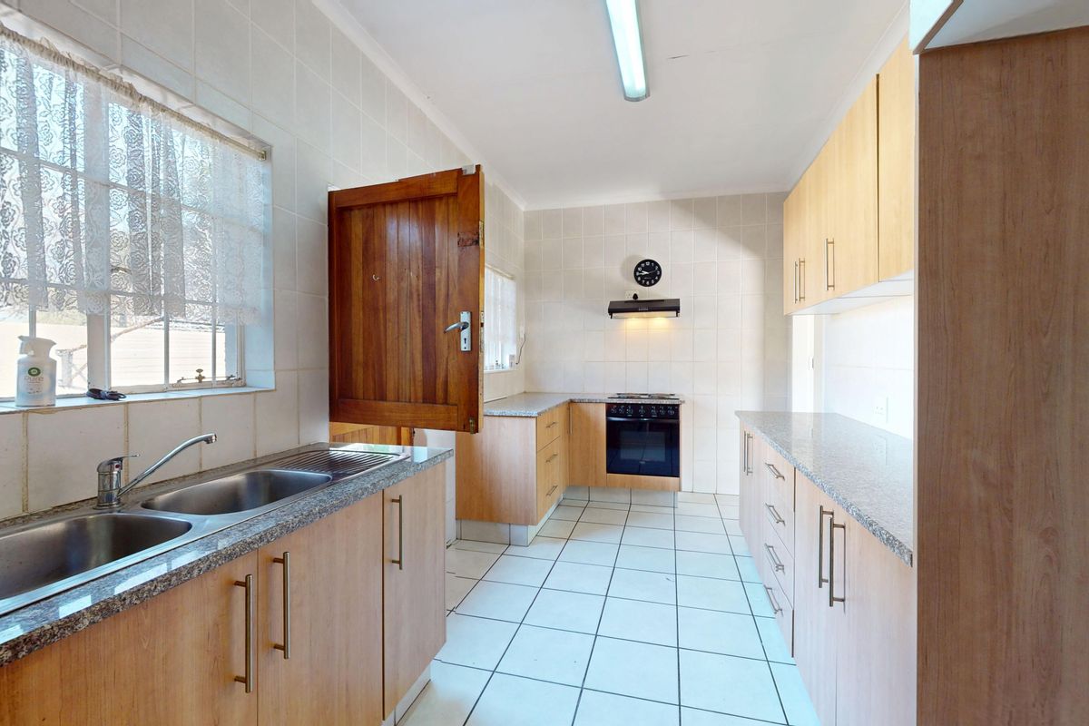 A functional kitchen featuring granite countertops, built-in wooden cabinetry, a built-in oven with extractor fan, and tiled finishes throughout.