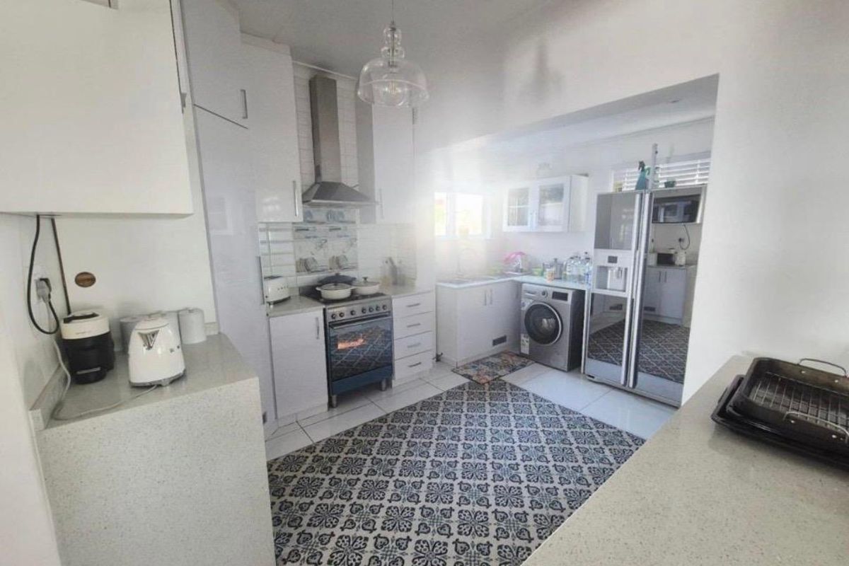 A functional kitchen featuring white cabinetry, stone countertops, integrated oven with extractor fan, and tiled flooring with a decorative pattern.