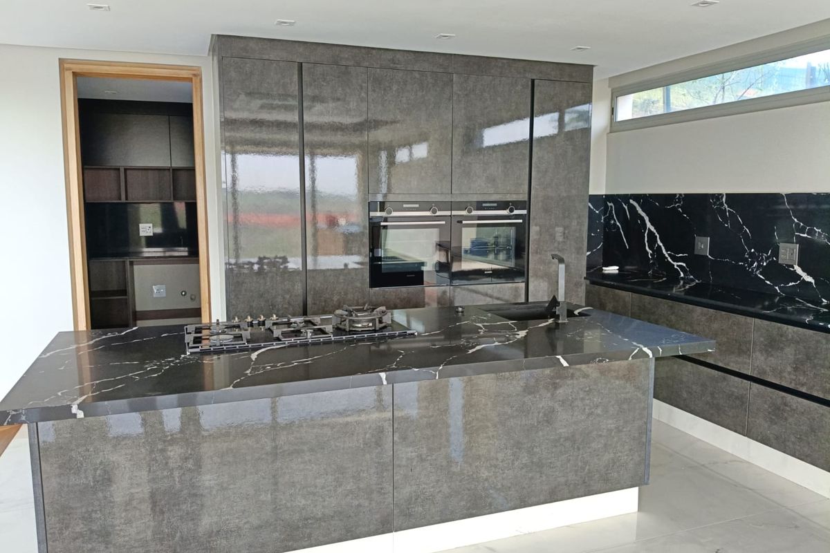 Modern kitchen featuring high-gloss cabinetry, a large island with a gas hob, marble-look stone countertops, and integrated double ovens.