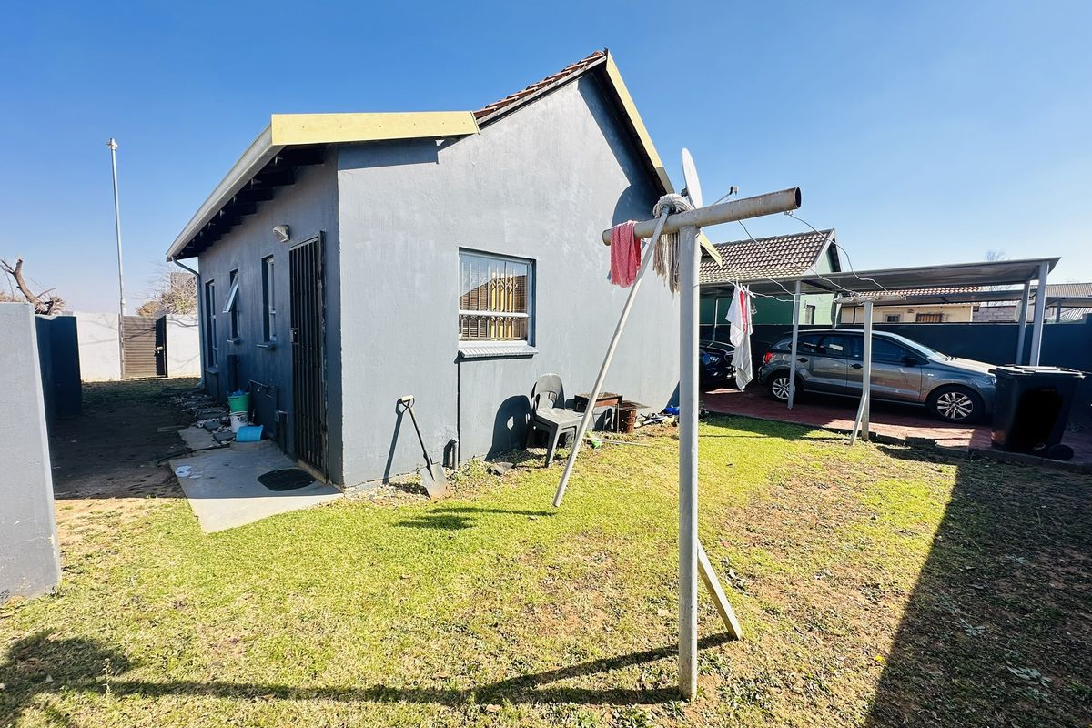 Rear view of the property featuring a grey exterior finish, security bars on windows, a carport, and a private backyard area.