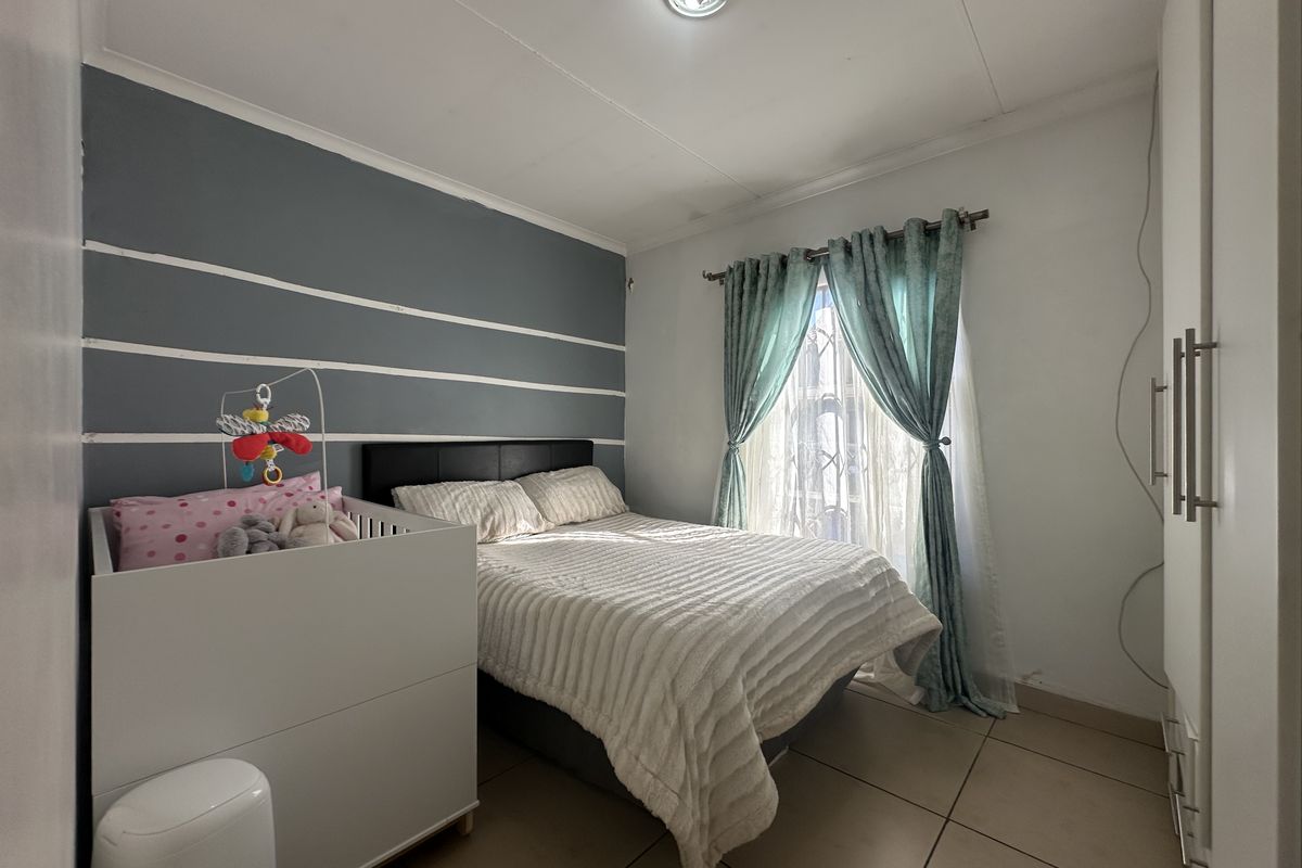 A functional bedroom featuring tiled flooring, built-in cupboards, and a feature wall, providing a practical space with potential for cosmetic updates.