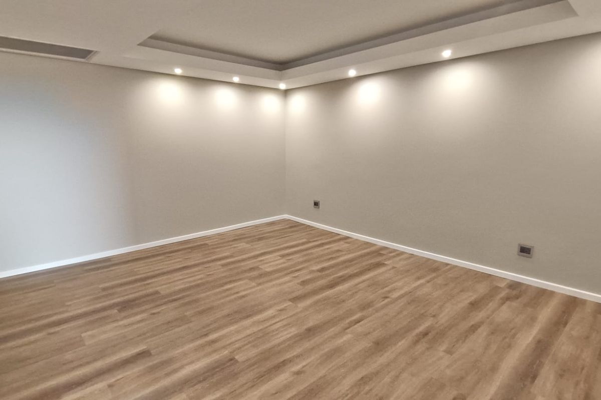 A bright, empty living room featuring modern laminate flooring, recessed ceiling lighting, and a clean, neutral aesthetic ready for furnishing.