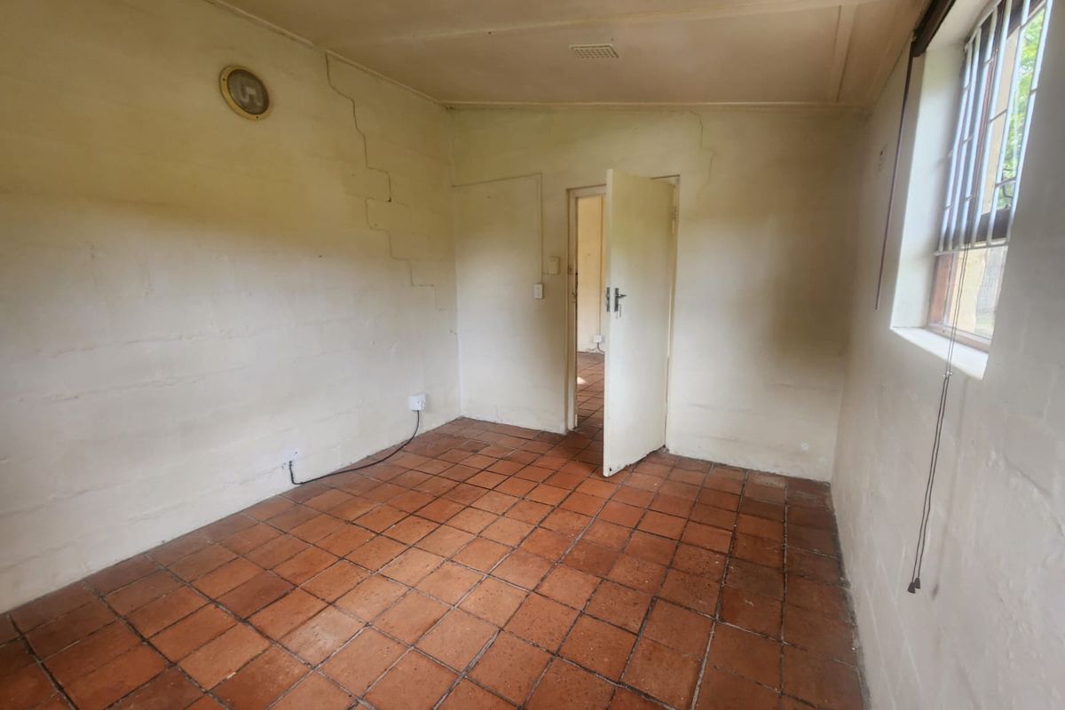 An empty bedroom featuring terracotta floor tiles, a security-barred window, and visible wall cracking requiring maintenance and cosmetic updates.
