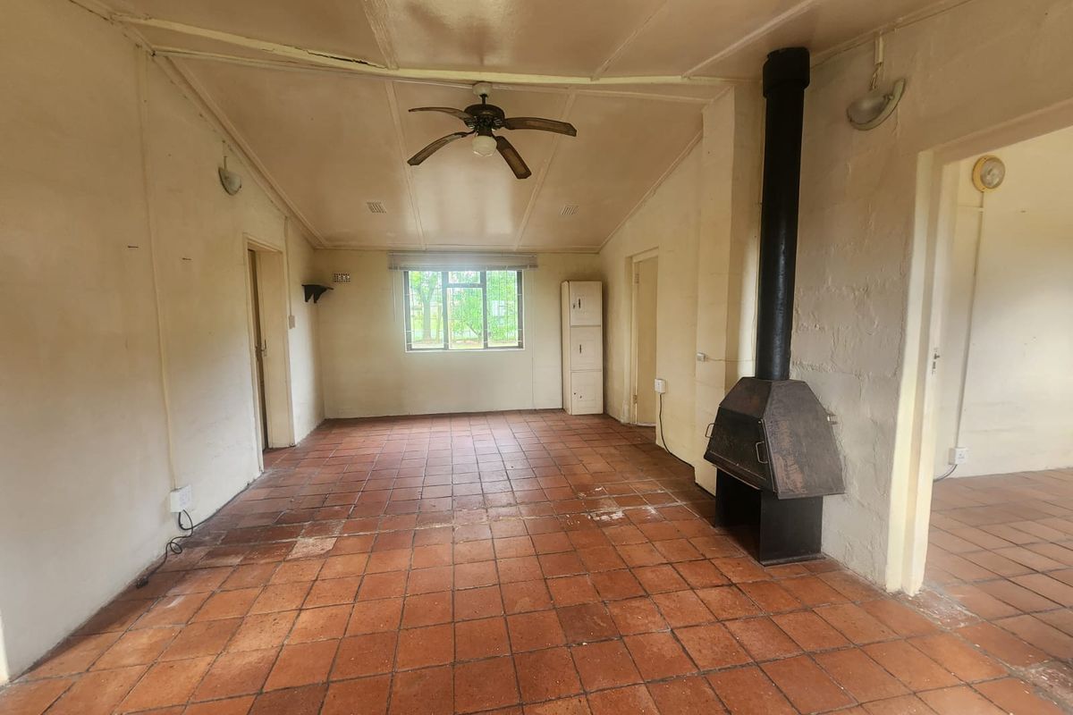 Spacious living area featuring terracotta floor tiles, a built-in fireplace, and a ceiling fan, offering a blank canvas for renovation.
