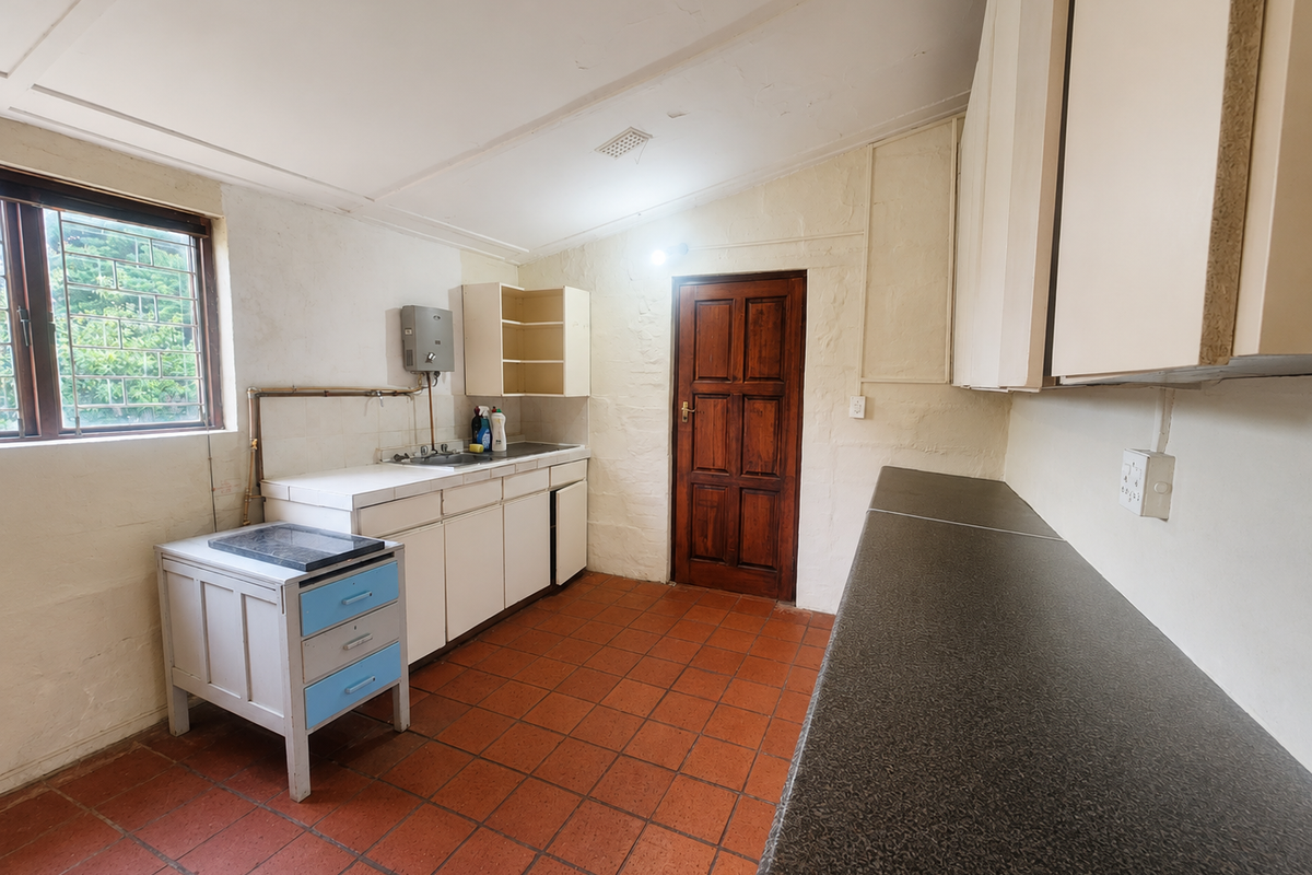 A dated kitchen featuring terracotta floor tiles, built-in cabinetry, a single sink, and a wooden door leading to the exterior.