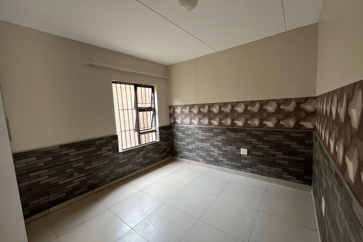 An empty bedroom featuring tiled flooring and decorative wall cladding with security bars on the window.