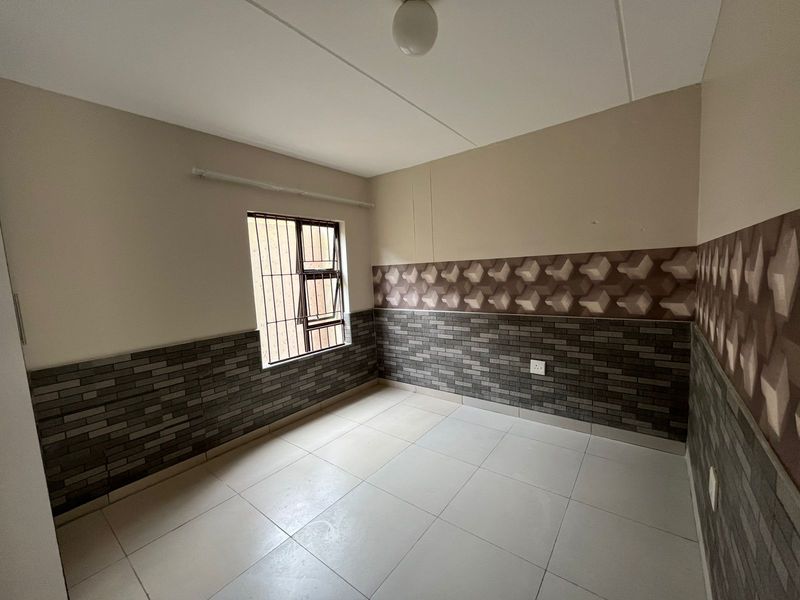 An empty bedroom featuring tiled flooring and decorative wall cladding with security bars on the window.