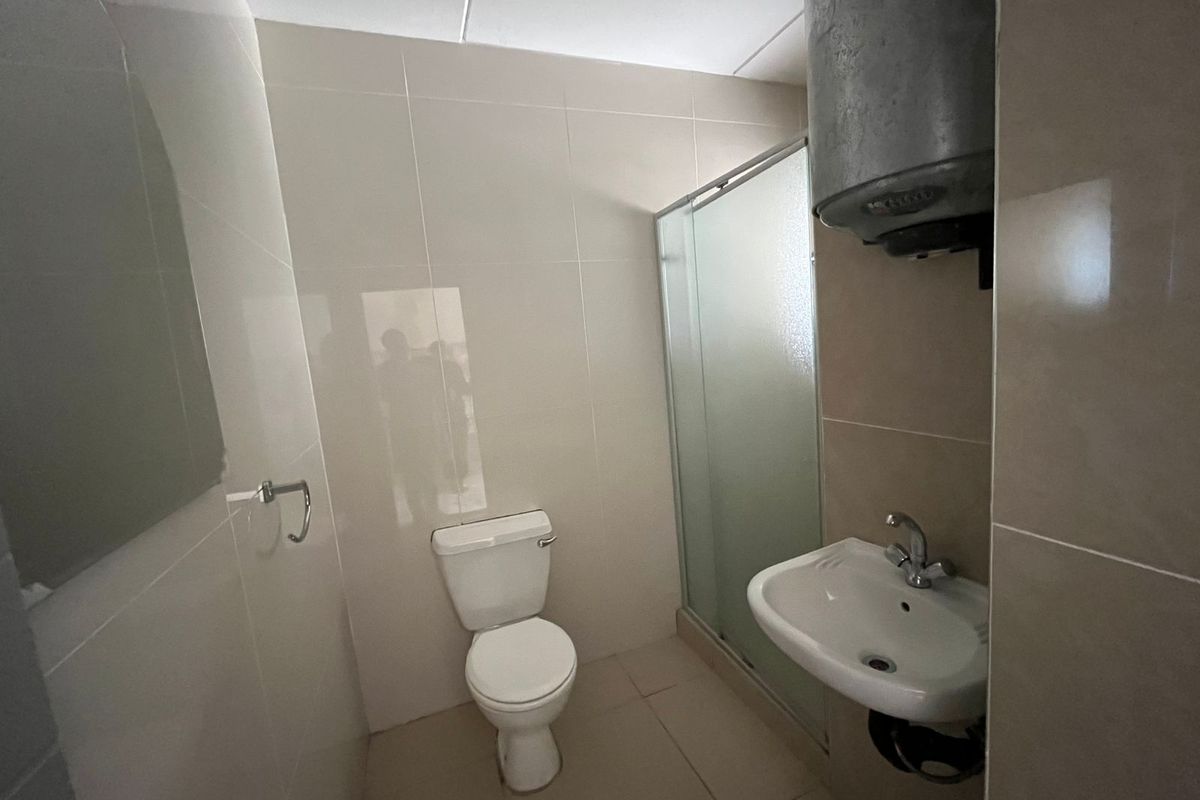 A functional bathroom featuring a shower enclosure, toilet, wall-mounted basin, and an exposed electric water heater with tiled finishes throughout.