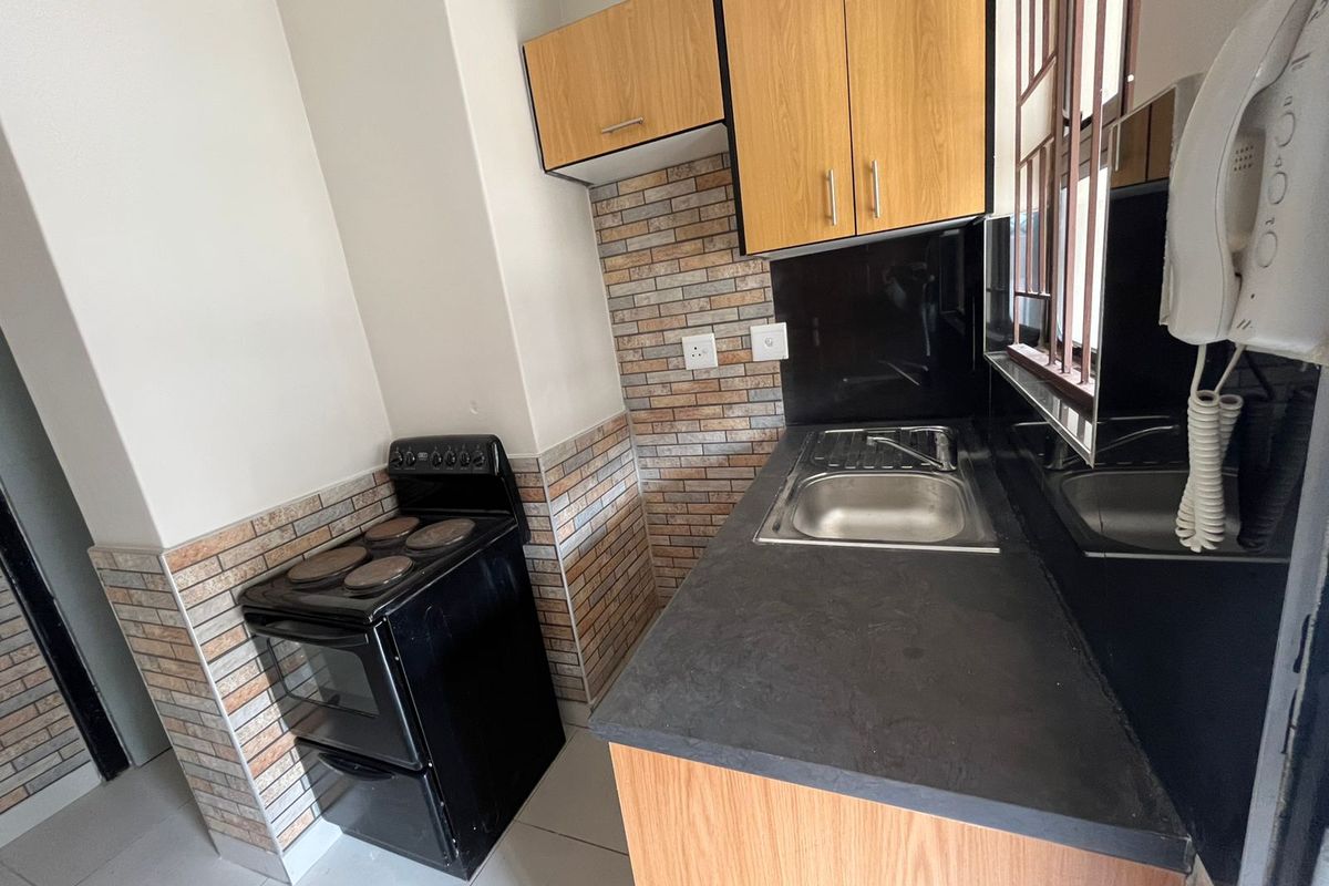 Compact kitchen featuring wood-finish cabinetry, black countertops, a stainless steel sink, and a built-in electric stove with a decorative tile backsplash.