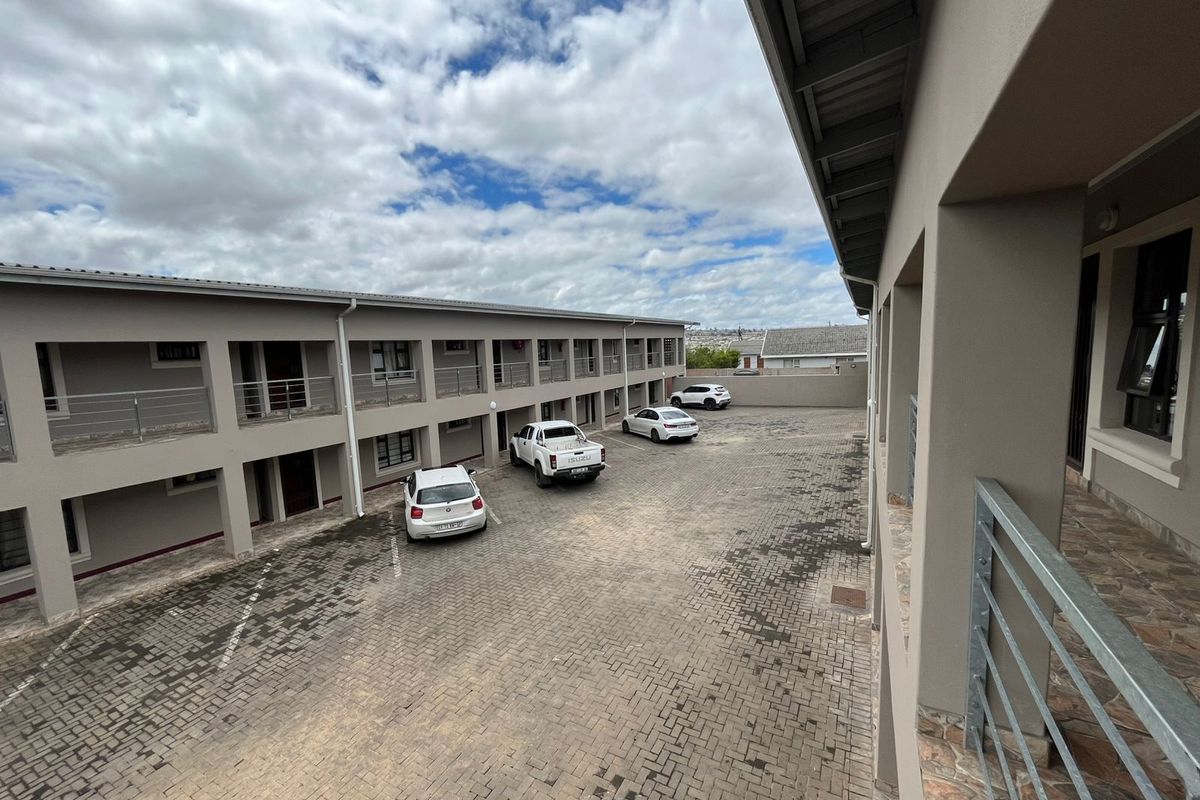 An elevated view of a paved apartment complex courtyard featuring multi-level covered walkways and metal safety railings.