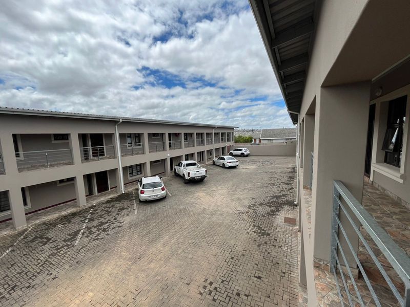 An elevated view of a paved apartment complex courtyard featuring multi-level covered walkways and metal safety railings.