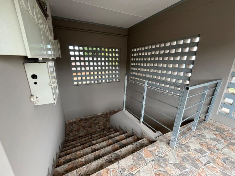 A functional stairwell area featuring tiled steps, a metal safety railing, and decorative breeze block ventilation panels.