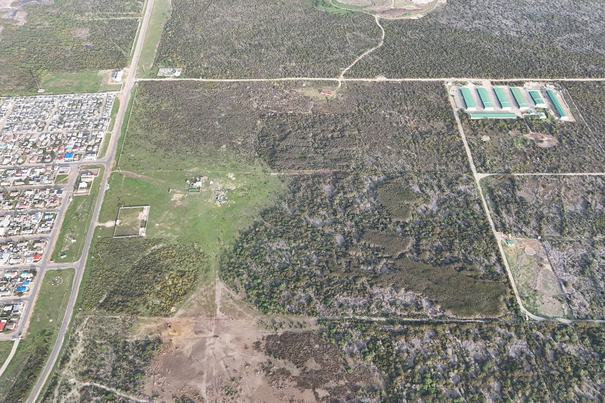 An aerial view of a large, undeveloped residential land parcel featuring natural vegetation and surrounding road access.