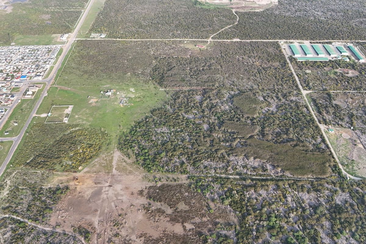 An aerial view of a large, undeveloped residential land parcel featuring natural vegetation and surrounding infrastructure.