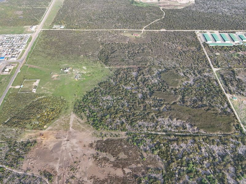 An aerial view of a large, undeveloped residential land parcel featuring natural vegetation and surrounding infrastructure.