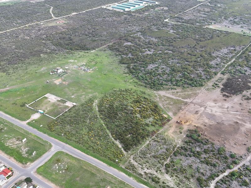 An aerial view of a large, undeveloped residential plot featuring natural vegetation, a fenced section, and direct access to the adjacent road.