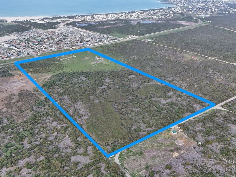 An aerial view of a large, undeveloped residential plot of land with clear boundary lines, situated near coastal residential areas.