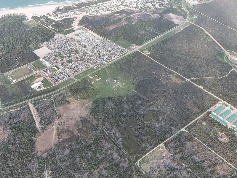An aerial view showing the surrounding coastal landscape, road infrastructure, and proximity to the nearby residential development.