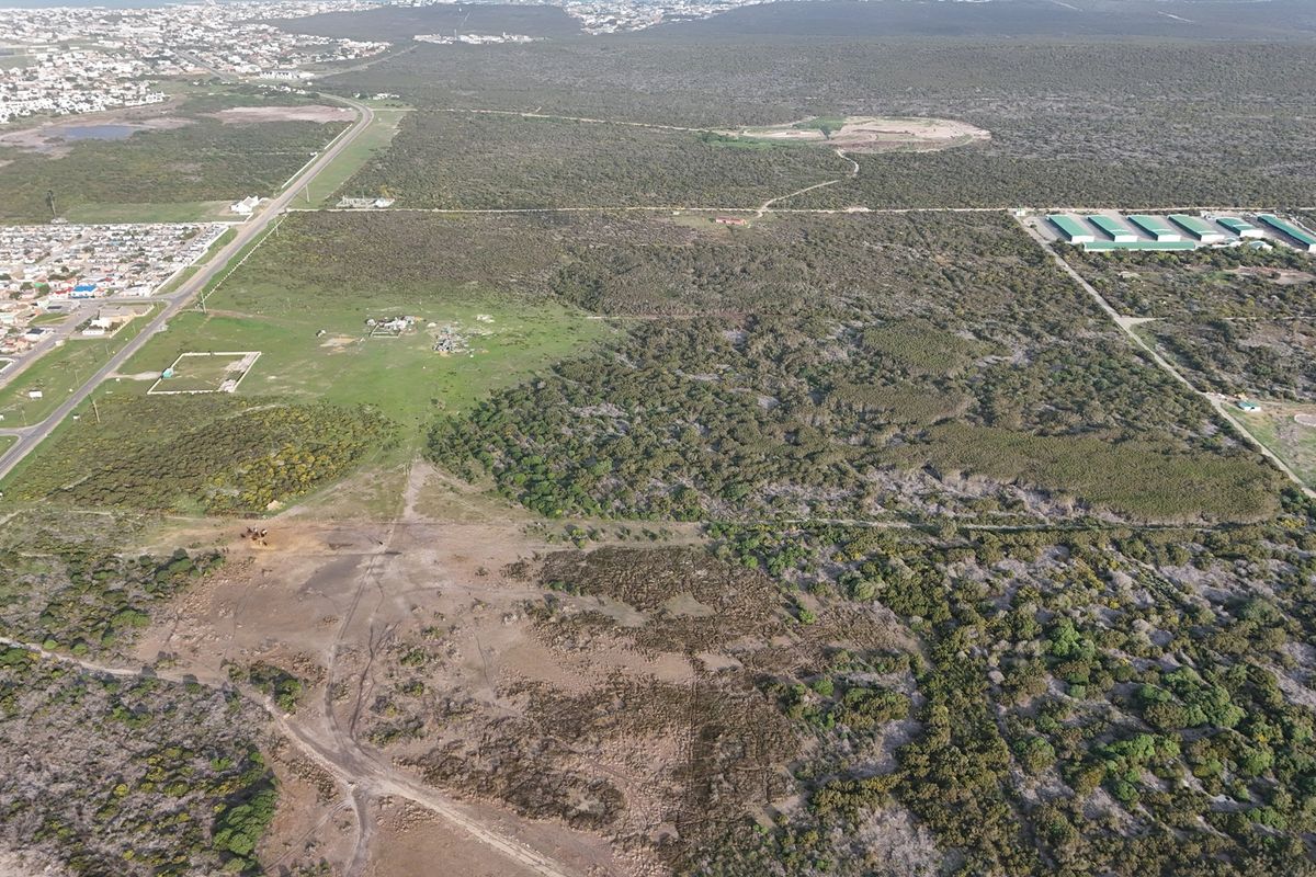 An aerial view of a large, undeveloped residential land parcel featuring natural vegetation and surrounding infrastructure.