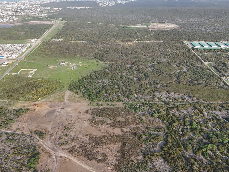 An aerial view of a large, undeveloped residential land parcel featuring natural vegetation and surrounding infrastructure.