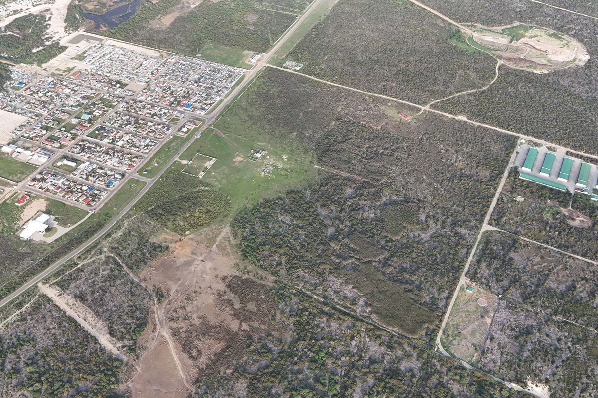 An aerial view of a large parcel of vacant residential land situated adjacent to an established residential neighborhood and rural landscape.