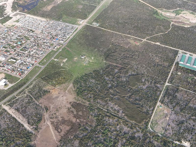 An aerial view of a large parcel of vacant residential land situated adjacent to an established residential neighborhood and rural landscape.
