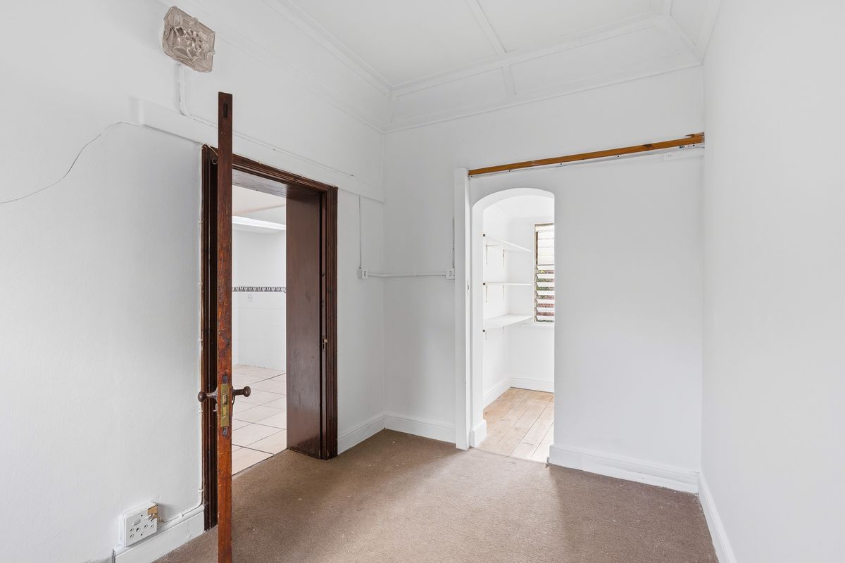 An empty bedroom featuring original coved ceilings, a timber door frame, and an adjoining walk-in storage area with built-in shelving.