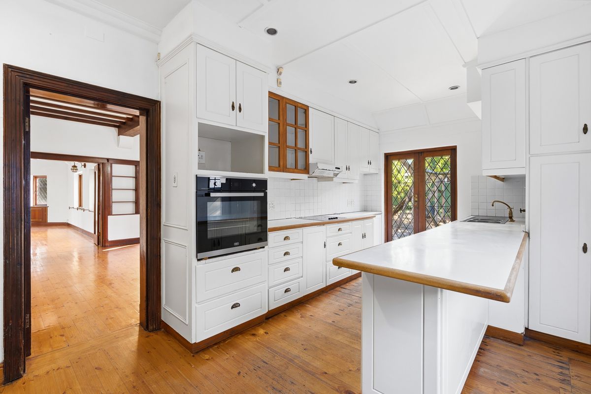 A bright, well-maintained kitchen featuring white cabinetry, built-in appliances, timber flooring, and direct access to the garden through glass doors.