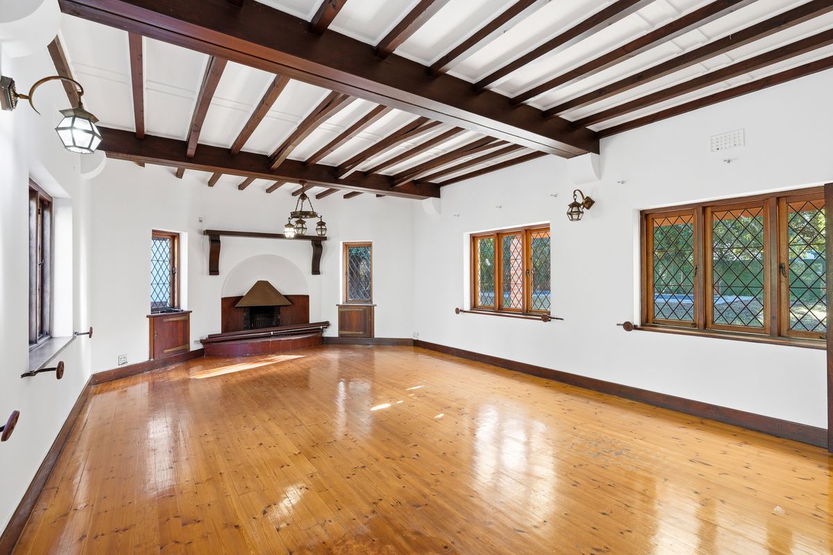 Spacious living room featuring exposed timber ceiling beams, polished timber flooring, leaded glass windows, and a characterful built-in fireplace.