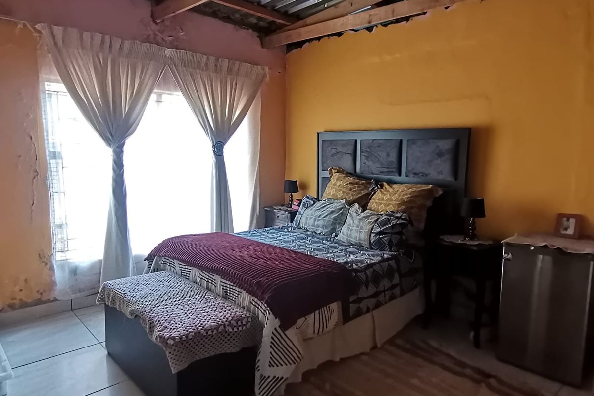 A bedroom featuring exposed timber roof trusses, corrugated metal ceiling, and tiled flooring, currently requiring cosmetic wall repairs and finishing.