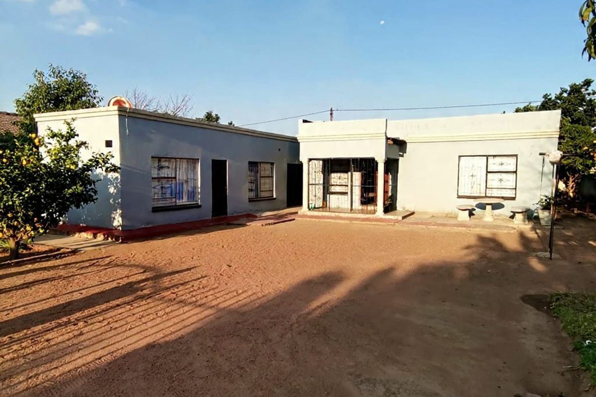 Rear view of a single-story residential property featuring a concrete patio area, security bars on windows, and a parapet roof design.
