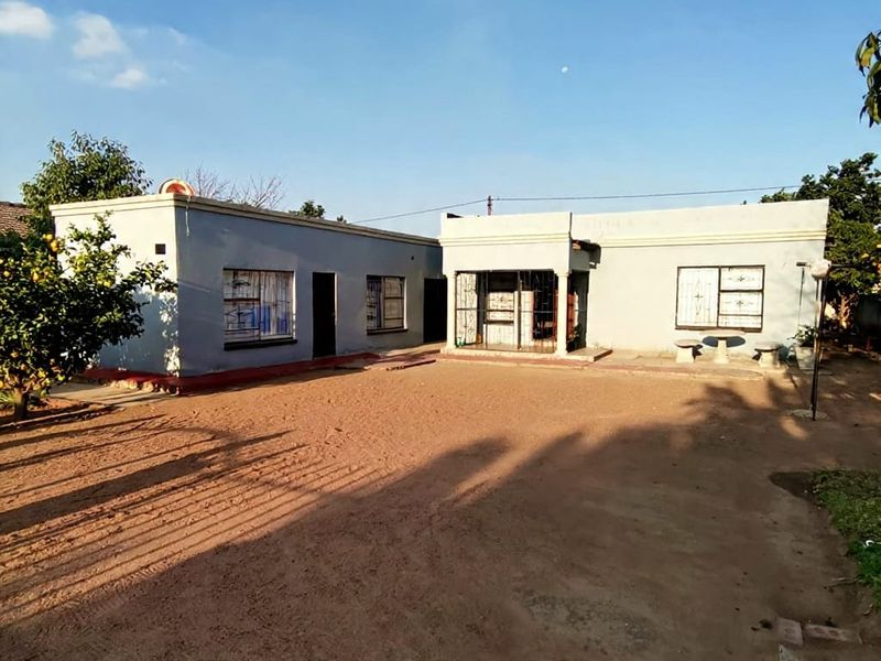 Rear view of a single-story residential property featuring a concrete patio area, security bars on windows, and a parapet roof design.