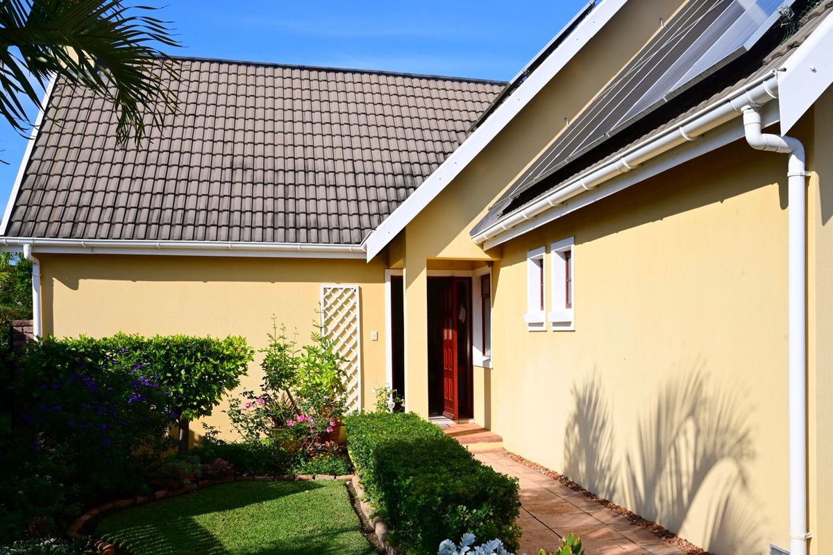A well-maintained rear exterior view of the house featuring a tiled roof, solar water heating panels, and a paved walkway leading to the entrance.