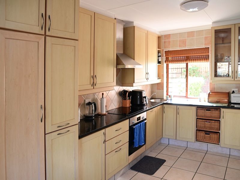 A functional kitchen featuring light wood cabinetry, granite countertops, a built-in oven with hob, and tiled flooring with a neutral backsplash.