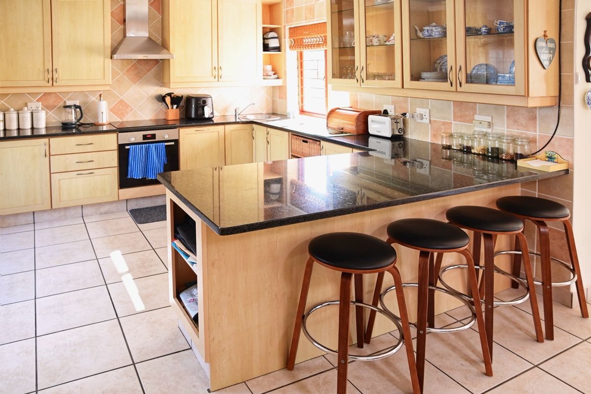 A functional kitchen featuring light wood cabinetry, dark granite countertops, a built-in oven, and a breakfast bar island with tiled flooring.