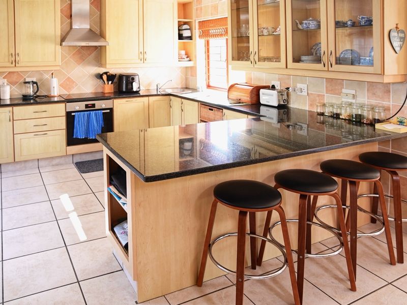 A functional kitchen featuring light wood cabinetry, dark granite countertops, a built-in oven, and a breakfast bar island with tiled flooring.