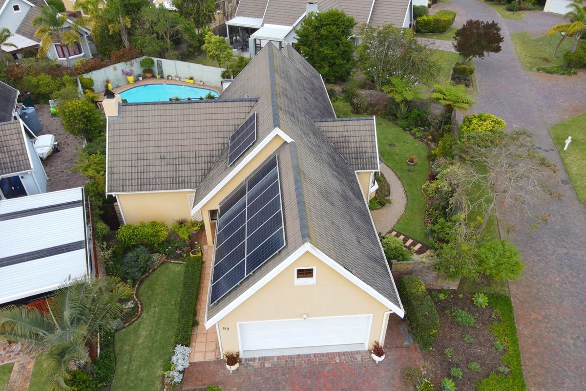 Aerial view of a residential property featuring a tiled roof with solar panels, a private swimming pool, landscaped gardens, and a paved driveway.
