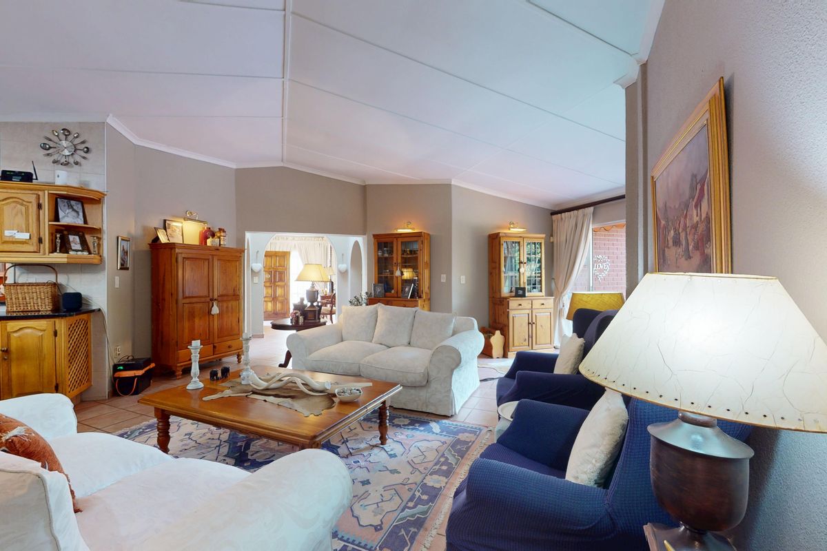 Spacious living room featuring tiled flooring, a vaulted ceiling, and built-in cabinetry, with an open archway leading to adjacent living areas.